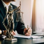 A close-up of a Lady Justice statue with legal materials on a desk in an office setting.
