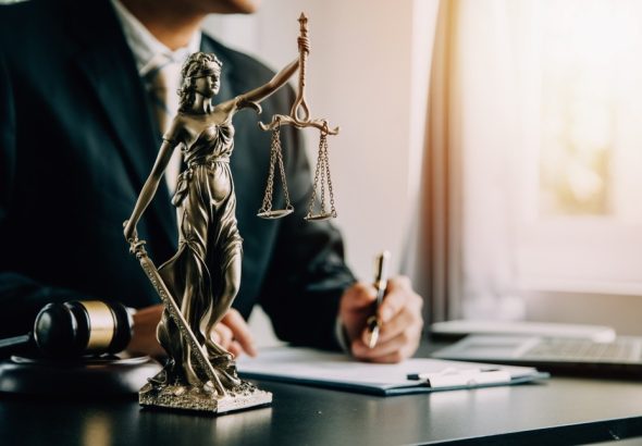 A close-up of a Lady Justice statue with legal materials on a desk in an office setting.