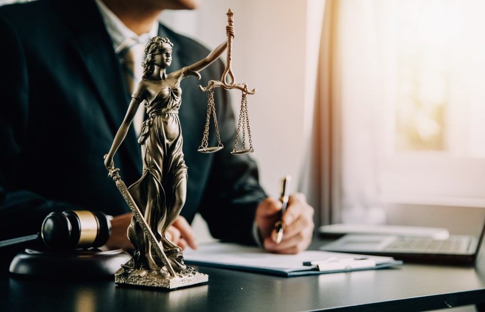A close-up of a Lady Justice statue with legal materials on a desk in an office setting.